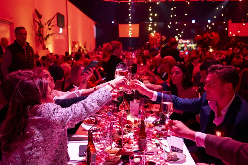 Gasten proosten aan een lange gedekte tafel tijdens een bedrijfsdiner